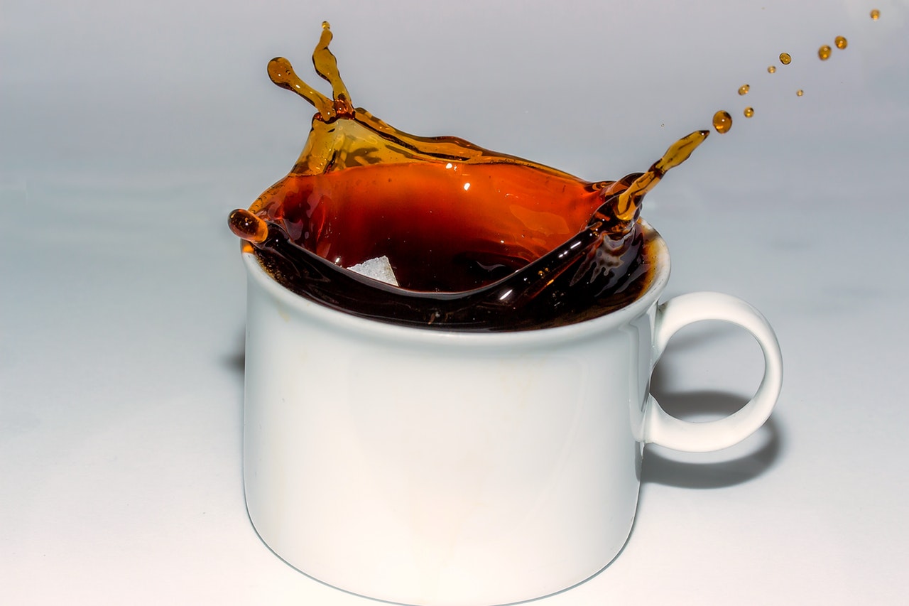 coffee splashing out as square sugar is falling inside the white mug