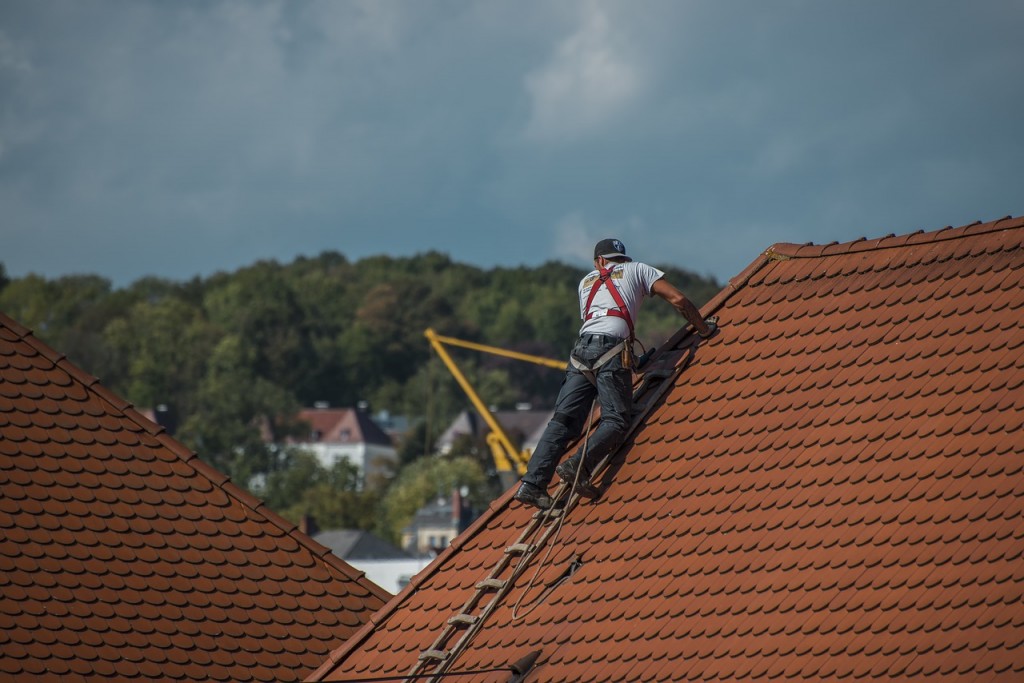 man with safety gear repairing house roof