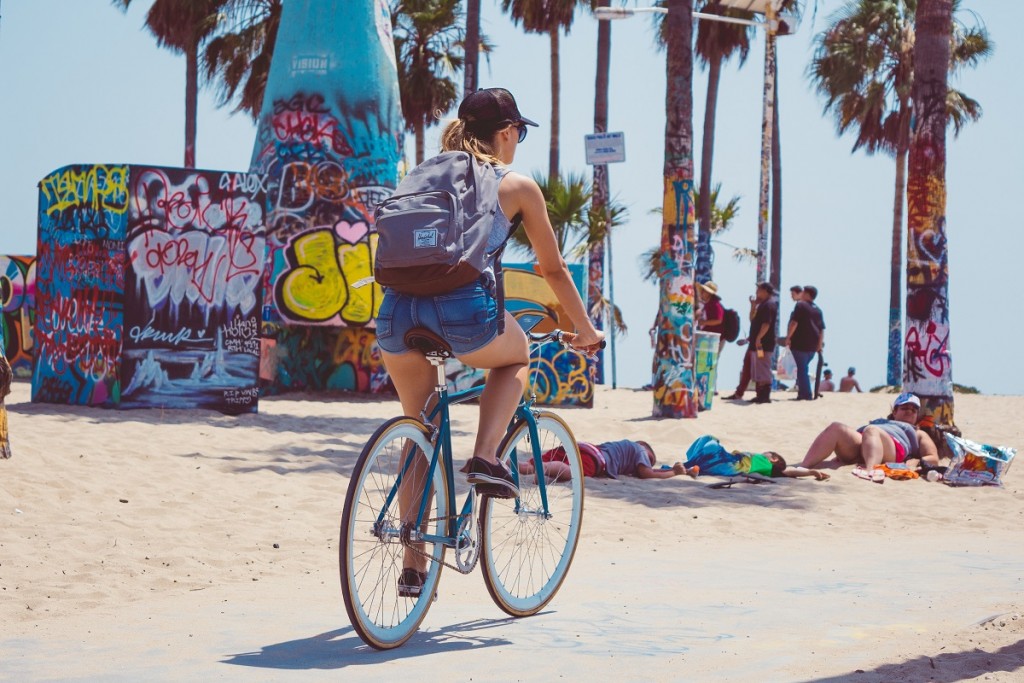 Female riding abike through the beach with a backpack