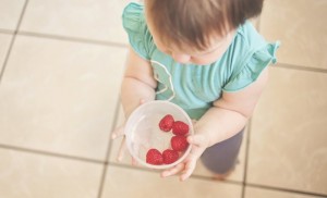 a toddler holding a white bowl with 5 strawberries in it