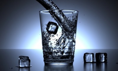 A glass of water in a deep blue background with ice cubes around ti