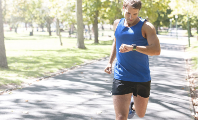 Man wearing blue tank top and black shorts jogging and checking his smartwatch
