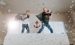 two boys on top of bed pillow fighting