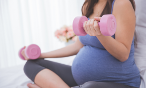 Pregnant lady sitting while lifting light pink drumbells