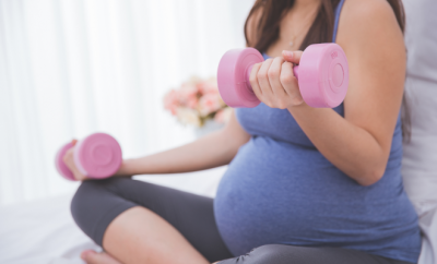 Pregnant lady sitting while lifting light pink drumbells