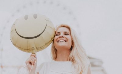 Blond woman holding a smiley ballon next to her