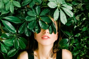 Woman hiding behind green leafy plant