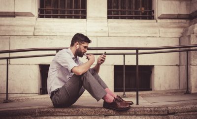 young man in business pants sitting on pavement on phone