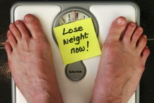 feet on weighing balance with a yellow sticker note "lose weight now"