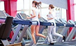 two women running on treadmills in a gym