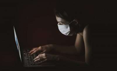 Woman in the dark wearing face mask in front of her laptop