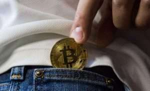 Close up of a Bitcoin being put inside a jeans pocket