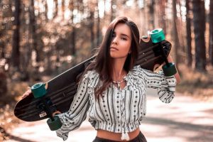 Young woman holding her skateboard on her shoulders