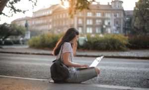 Young woman sitting by the side of the road on her laptop
