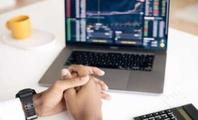 Man's hands folded while looking at stock trade in laptop