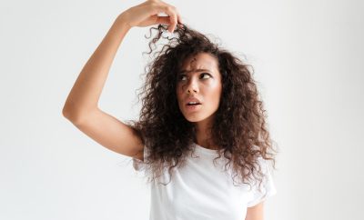 Portrait of a confused young woman examining her hair while standing isolated over white background