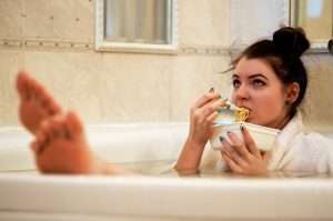 Lady in a bathtub eating noodles