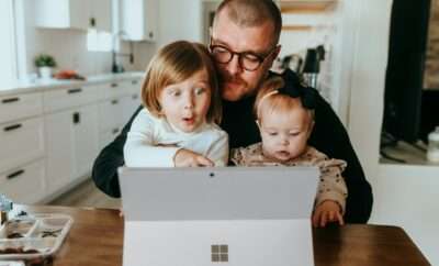 Dad with his toddlers on is lap and working on laptop