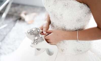 Bride holding her white, sparkling shoes in her hand